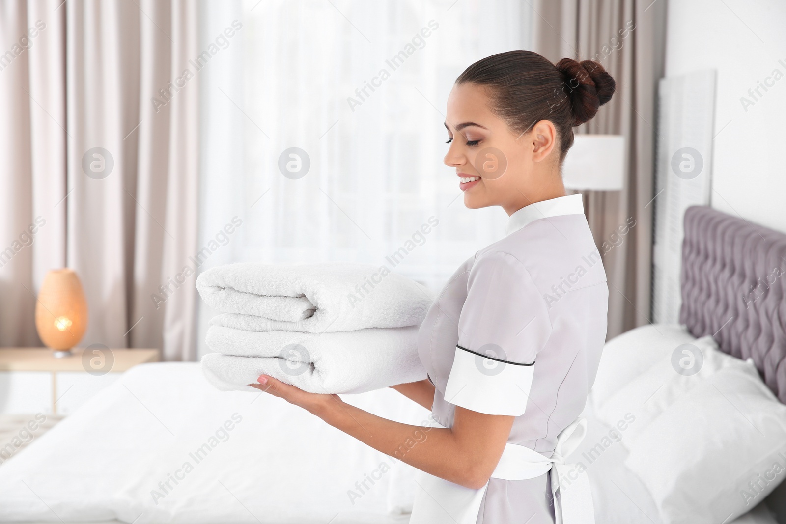 Photo of Young chambermaid with clean towels in bedroom