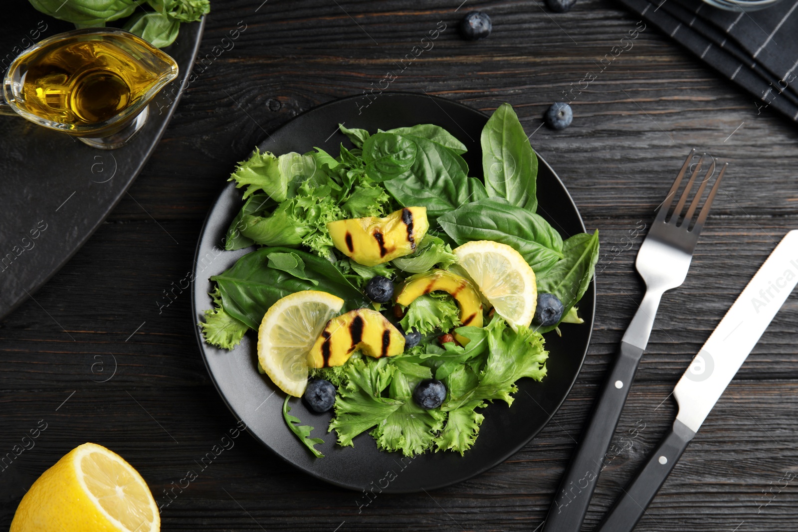 Photo of Delicious avocado salad with lemon and blueberries on black wooden table, flat lay