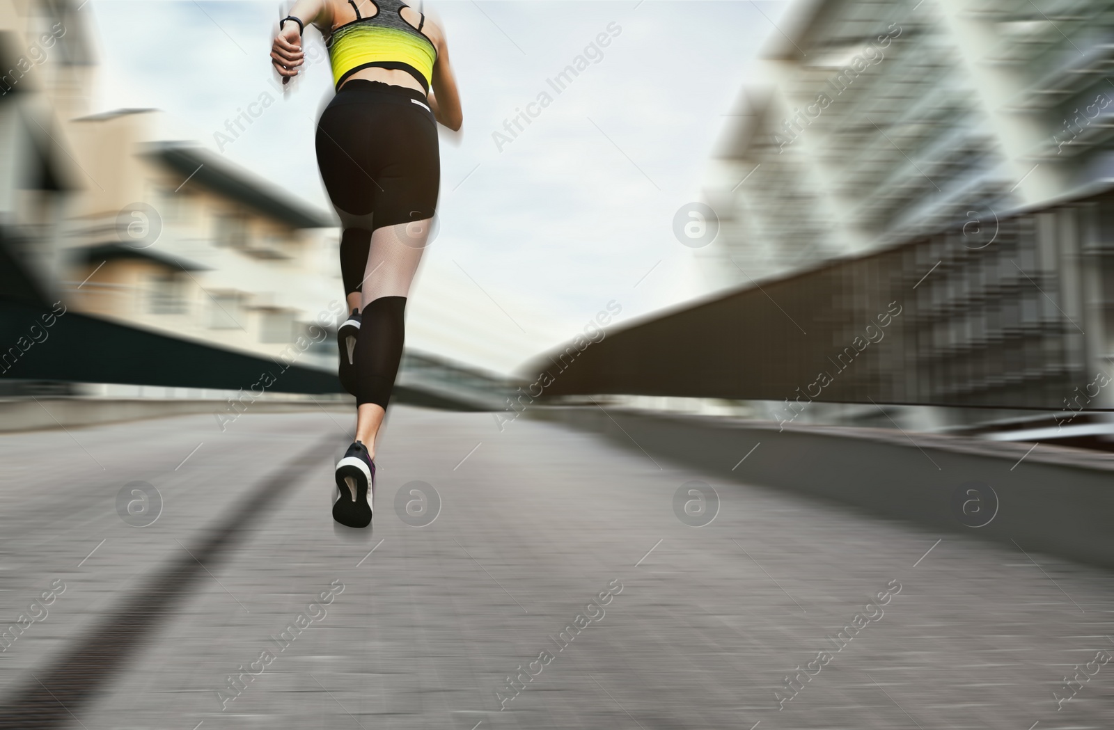 Image of Sporty young woman running on street, low angle view. Motion blur effect showing her speed