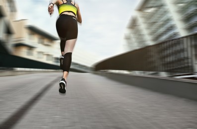Image of Sporty young woman running on street, low angle view. Motion blur effect showing her speed