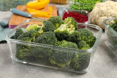 Photo of Glass container with broccoli on light gray table, closeup. Food storage