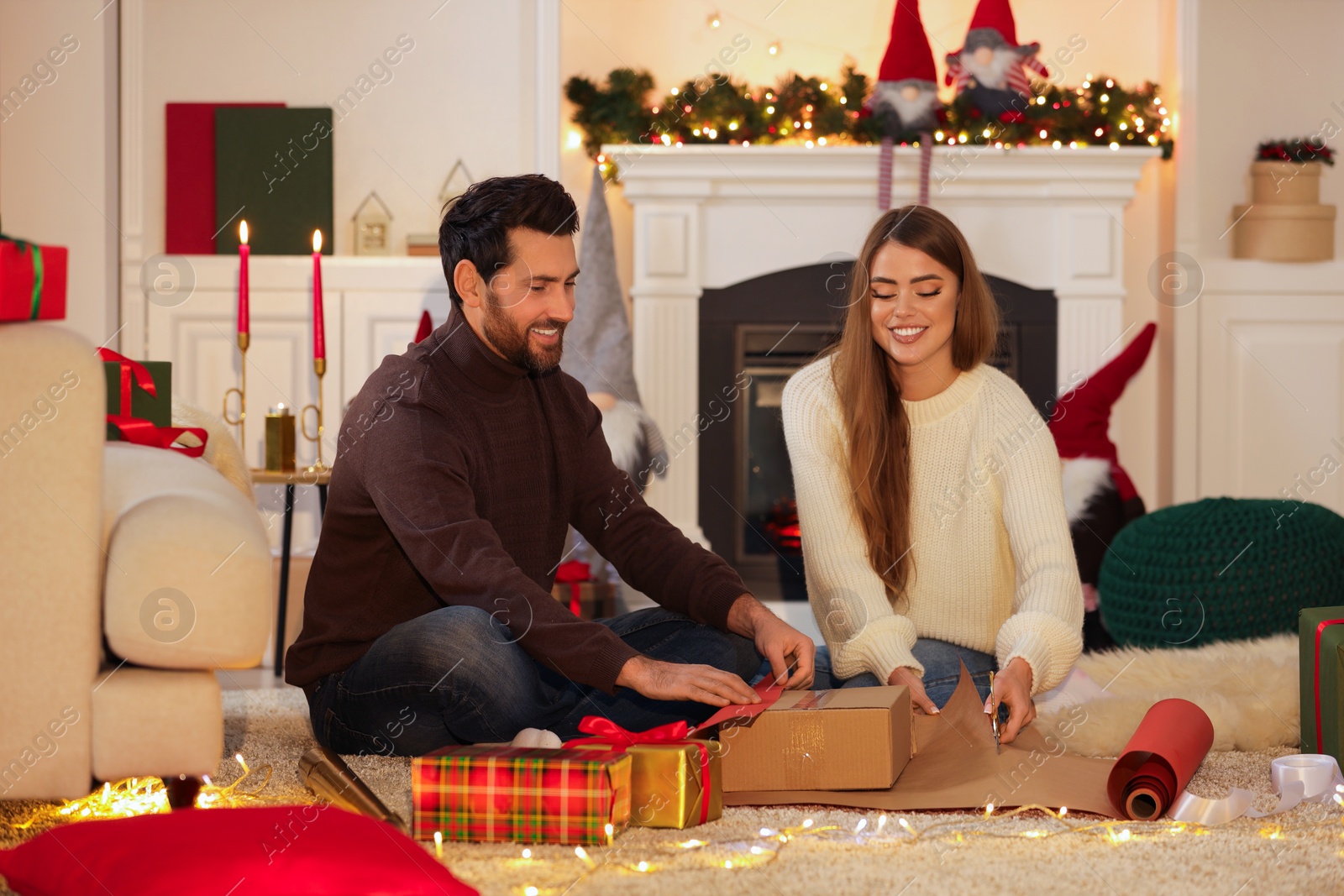 Photo of Happy couple decorating Christmas gift with wrapping paper at home