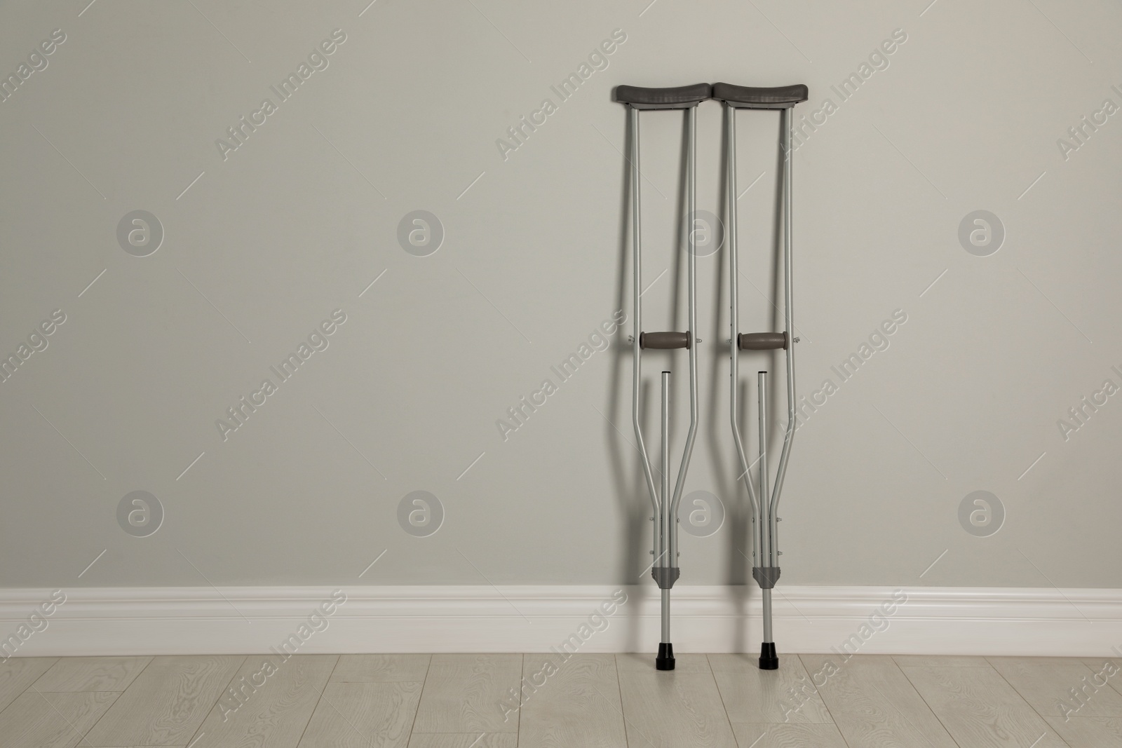 Photo of Pair of axillary crutches near light grey wall. Space for text
