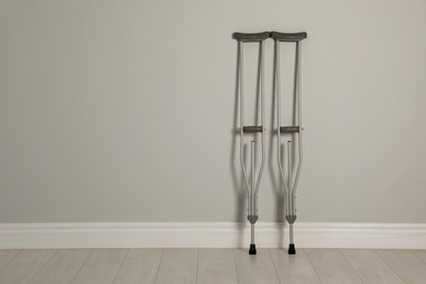 Pair of axillary crutches near light grey wall. Space for text