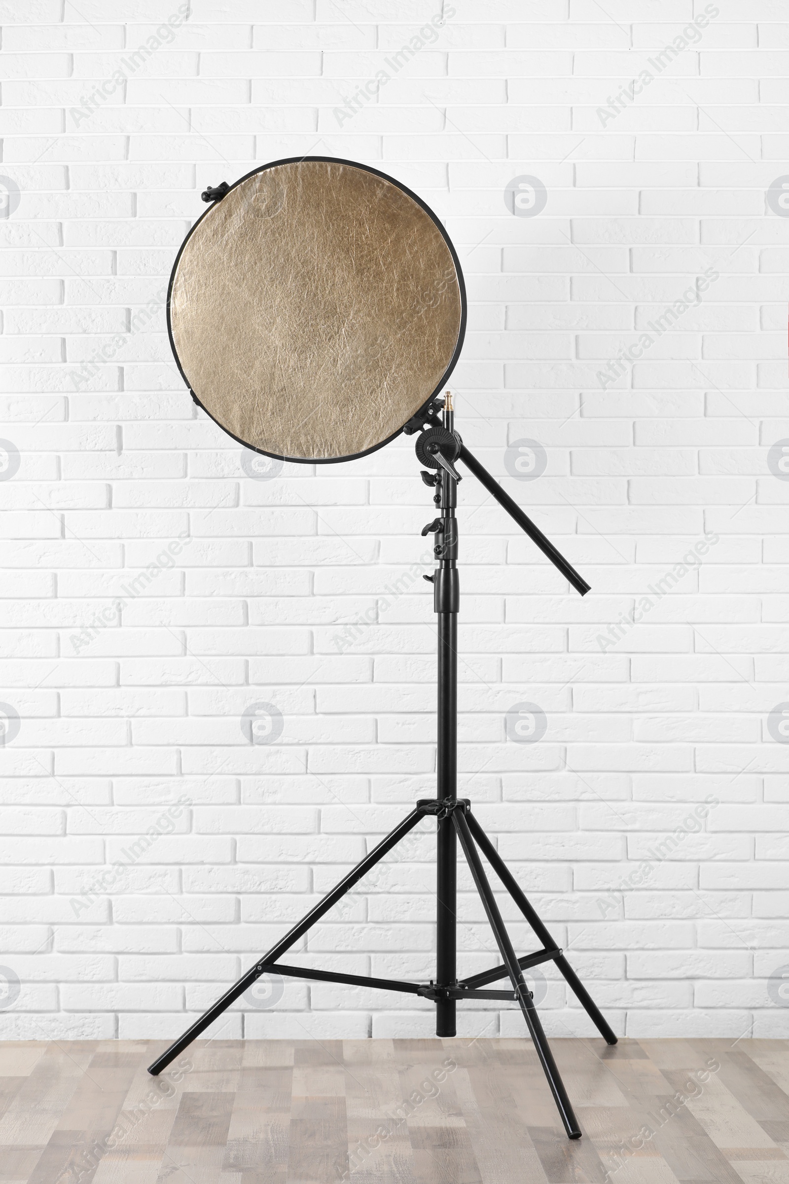 Photo of Professional golden reflector on tripod near white brick wall in room. Photography equipment