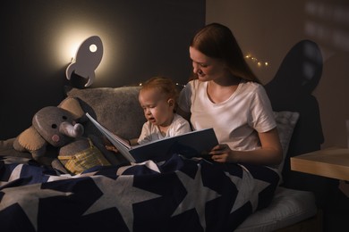 Mother and child reading book in room with rocket shaped night lamp