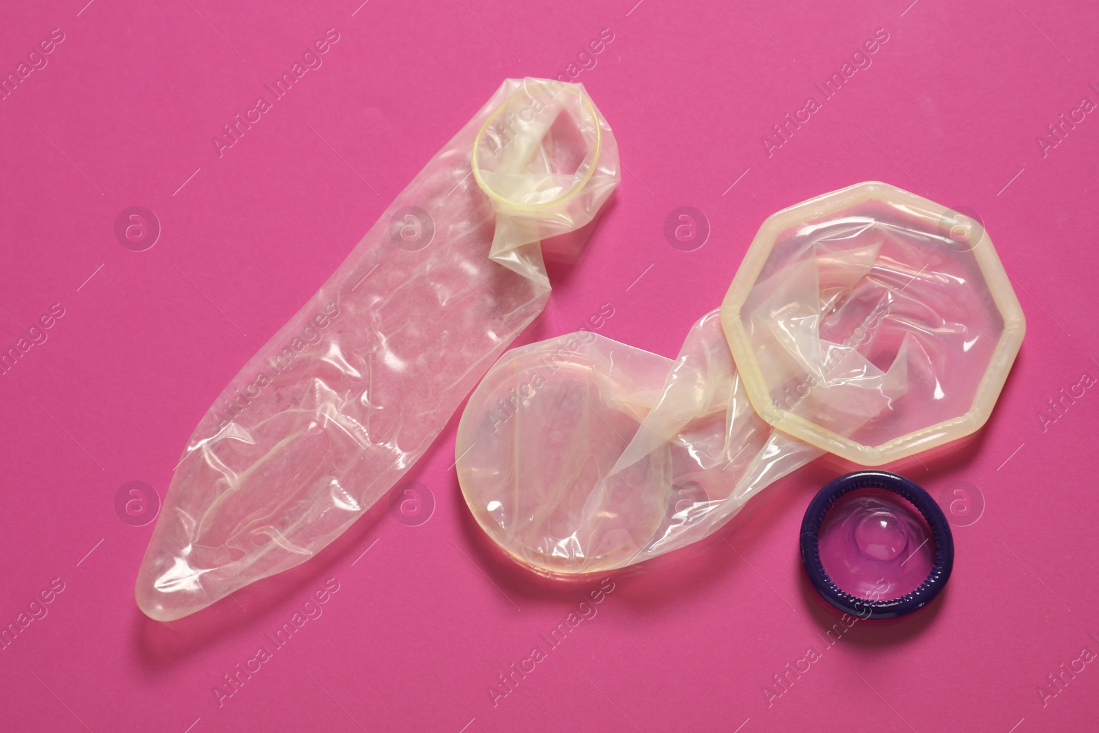 Photo of Unrolled female and male condoms on pink background, flat lay. Safe sex