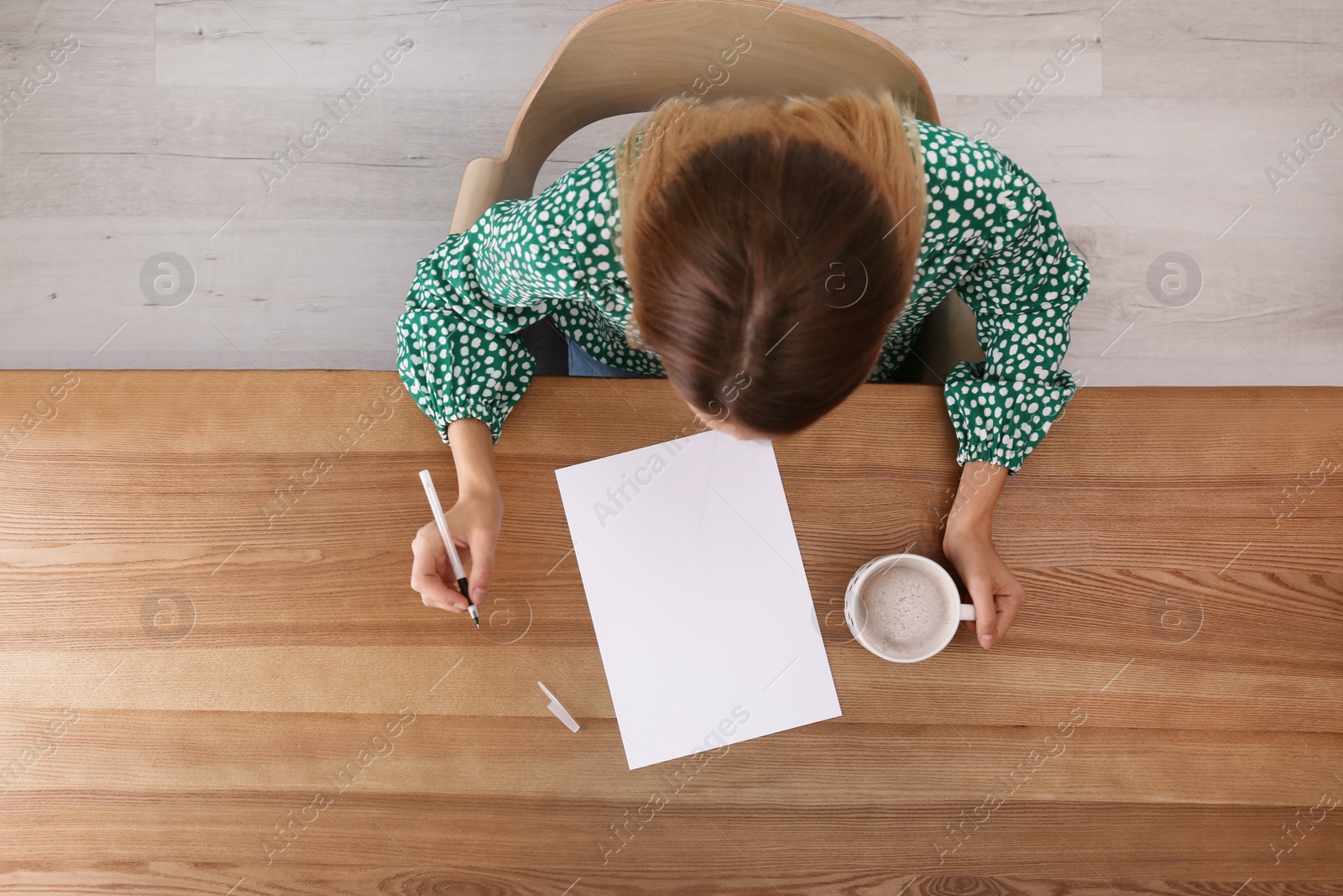 Photo of Woman writing on sheet of paper at table indoors, top view