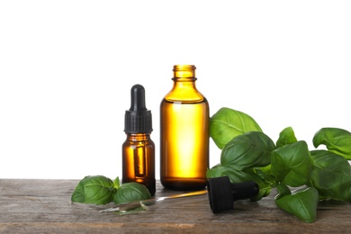 Photo of Bottles of basil essential oil on wooden table against white background