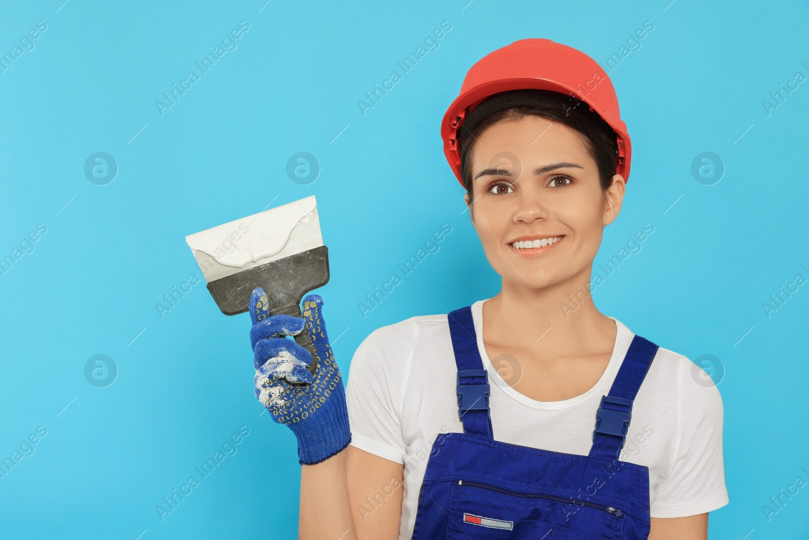 Photo of Professional worker in hard hat with putty knife on light blue background