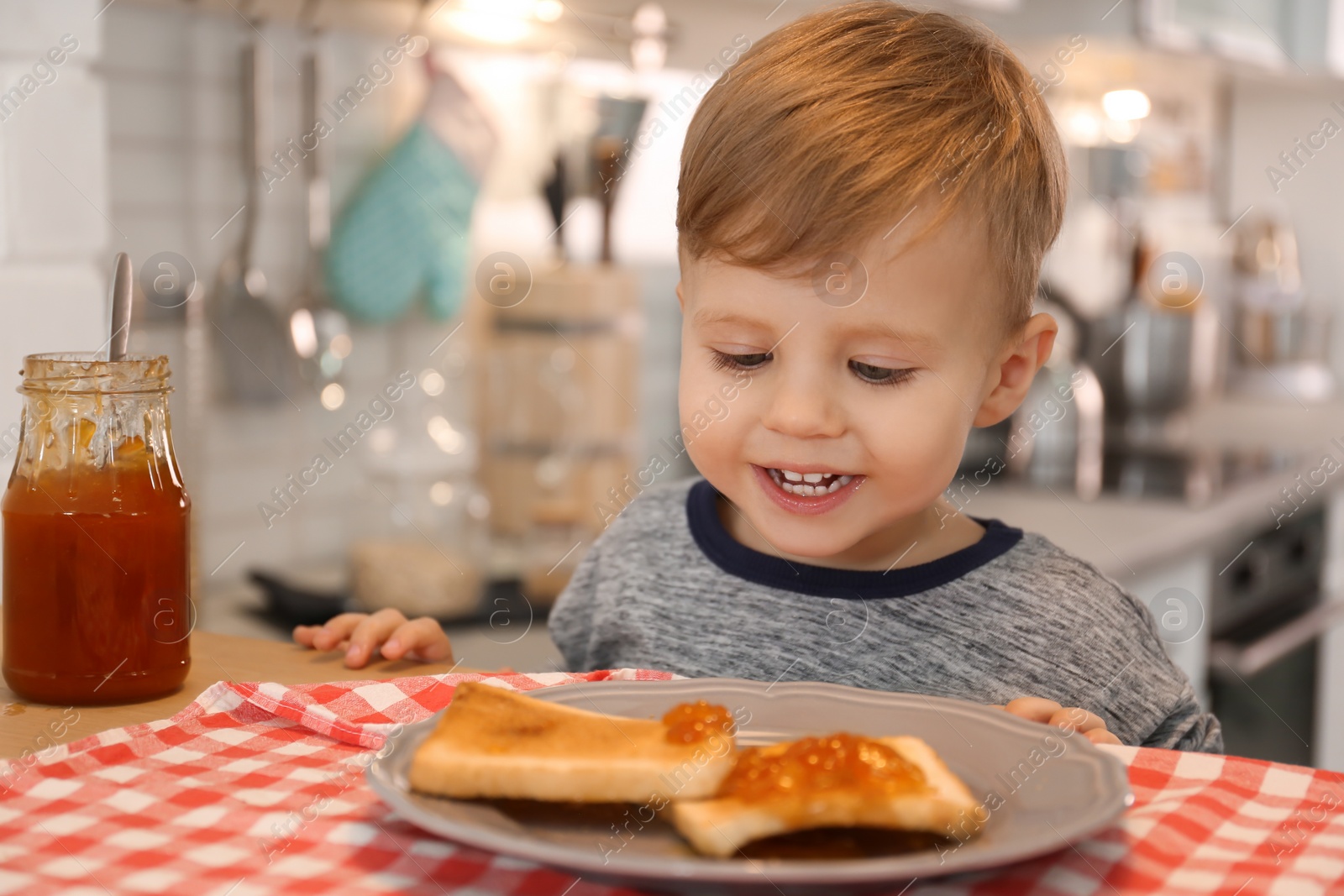 Photo of Little boy having breakfast with toast bread and jam at table in kitchen