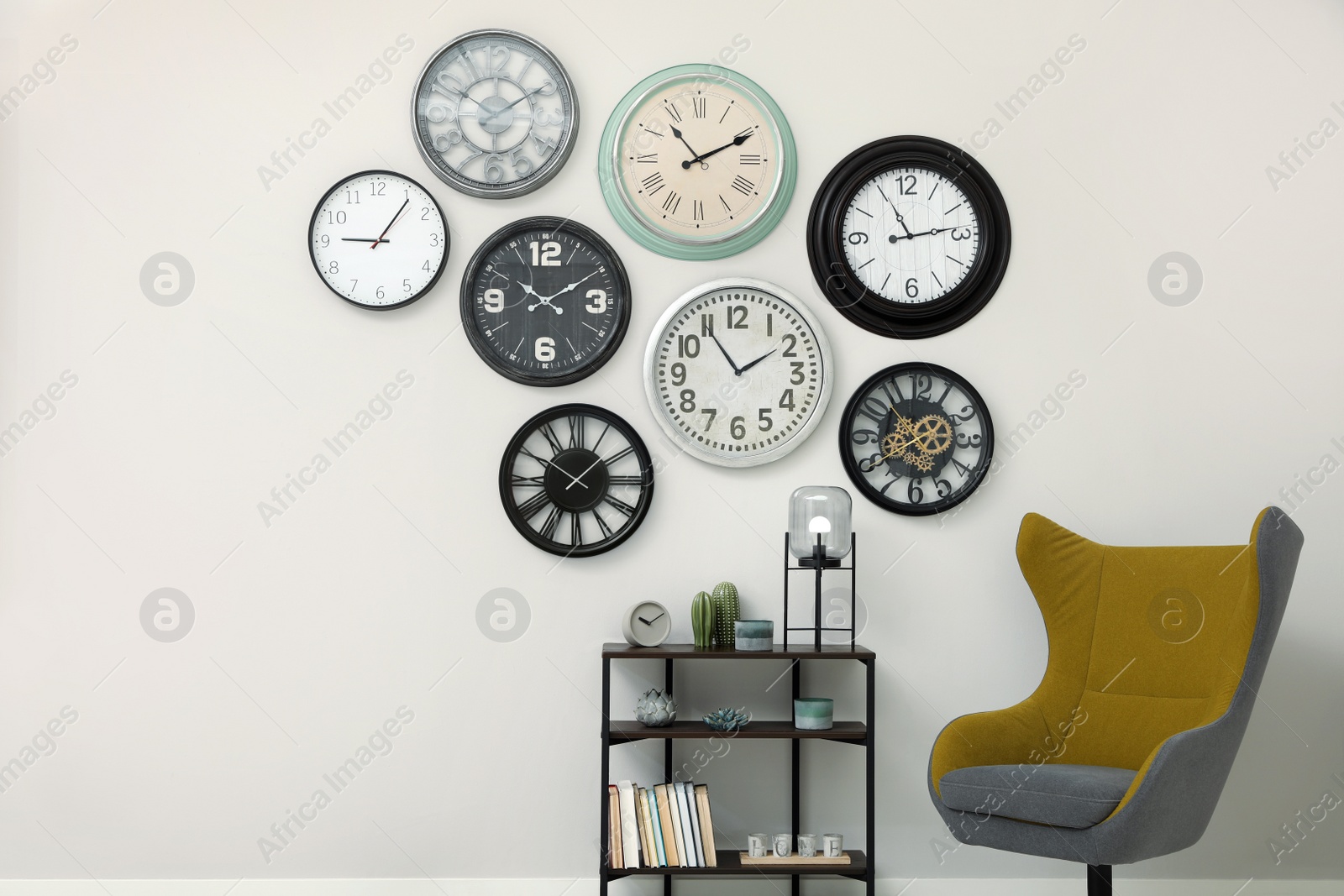 Photo of Armchair, console table and many different clocks hanging on white wall in room