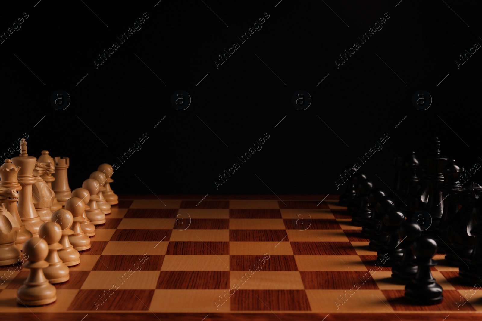 Photo of Many chess pieces on wooden checkerboard against black background, space for text