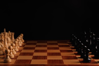 Many chess pieces on wooden checkerboard against black background, space for text