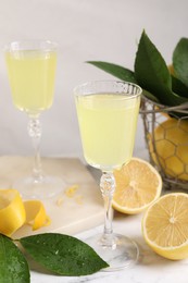 Photo of Tasty limoncello liqueur, lemons and green leaves on table