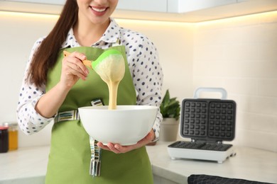 Woman preparing dough near Belgian waffle maker in kitchen, closeup