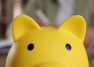 Photo of Yellow piggy bank on blurry background, closeup