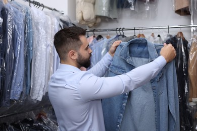 Dry-cleaning service. Worker holding denim shirt indoors