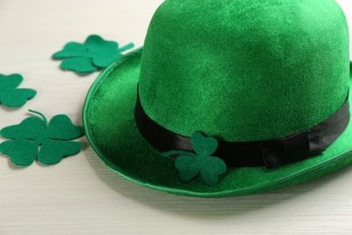 Leprechaun hat and decorative clover leaves on white wooden table, closeup. St Patrick's Day celebration