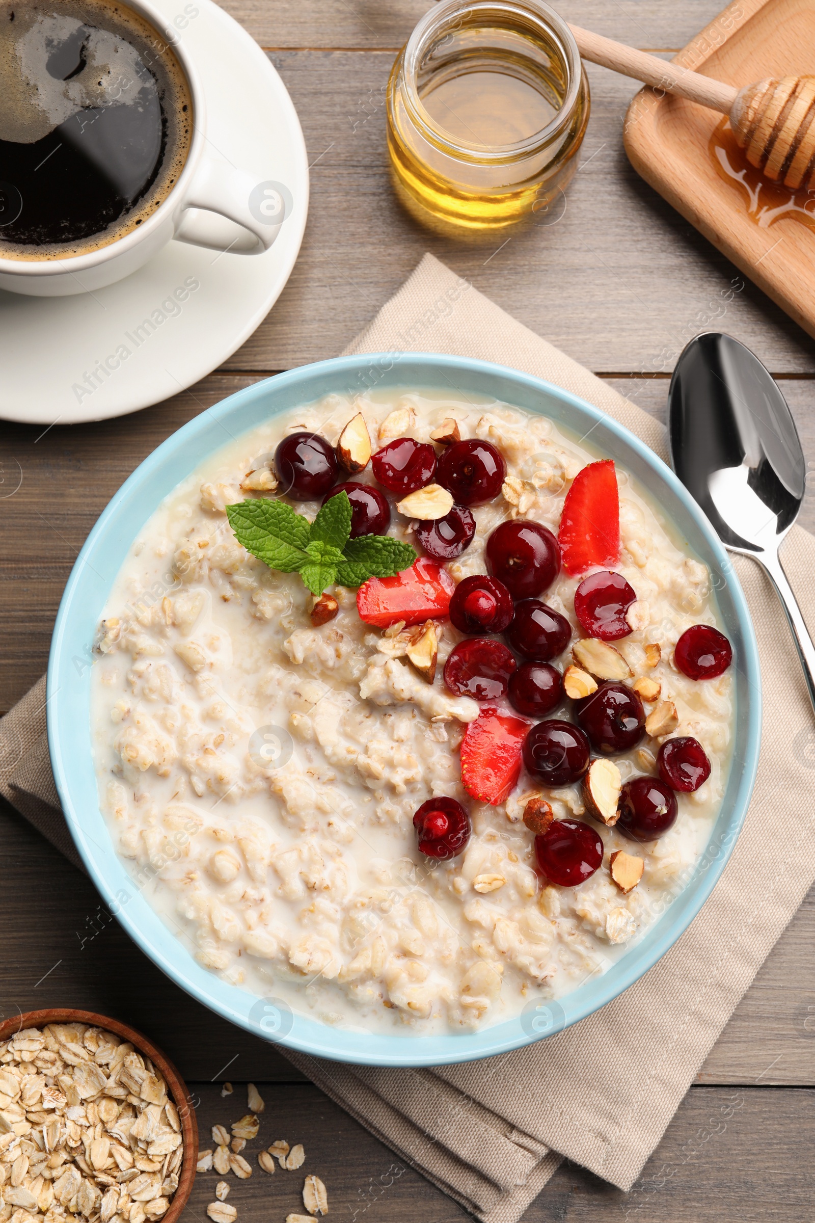 Photo of Bowl of oatmeal porridge served with berries on wooden table, flat lay