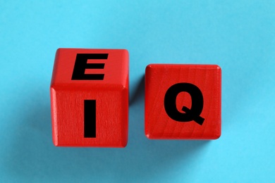 Photo of Red cubes with letters E, I and Q on light blue background, flat lay