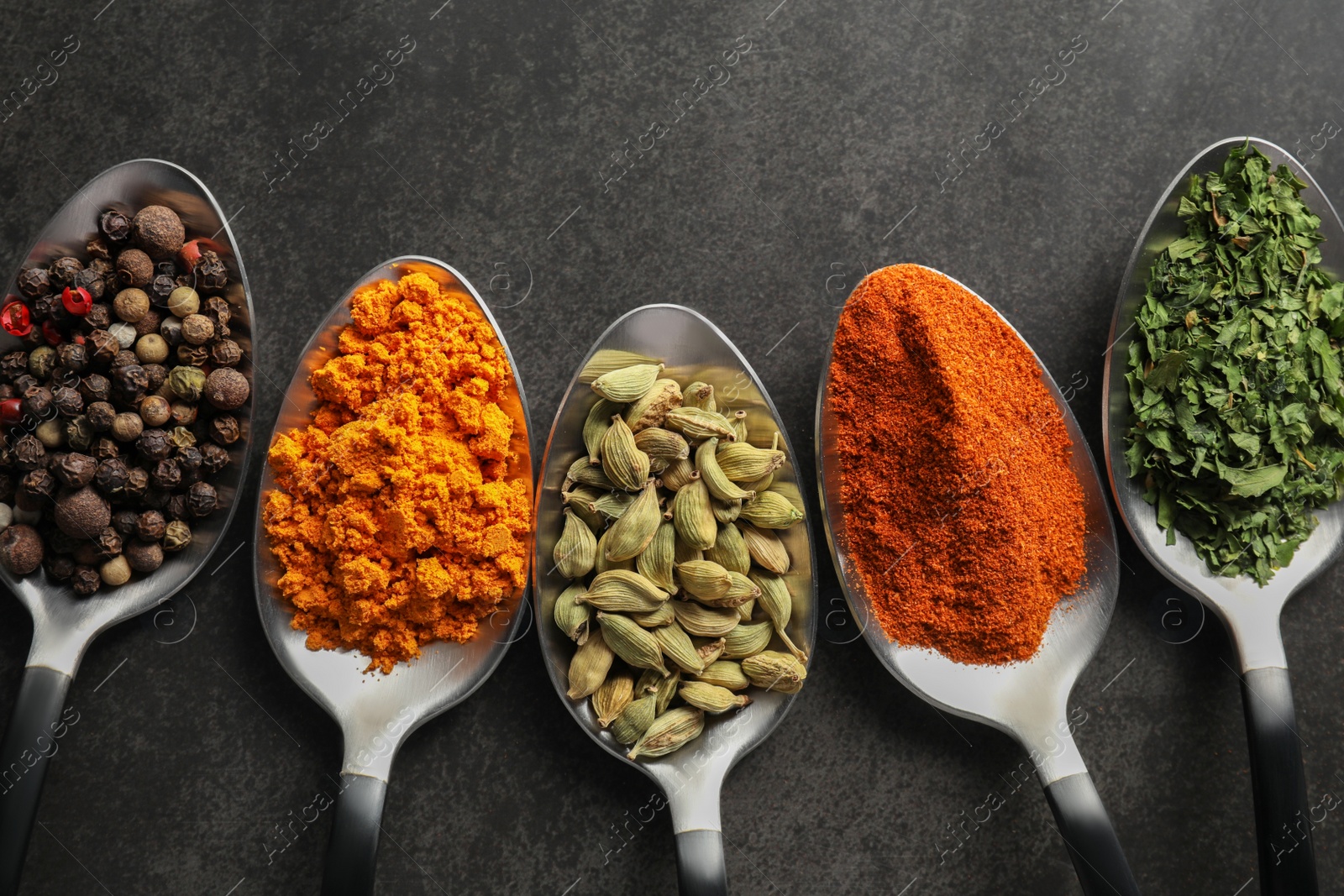 Photo of Metal spoons with different spices on black table, flat lay