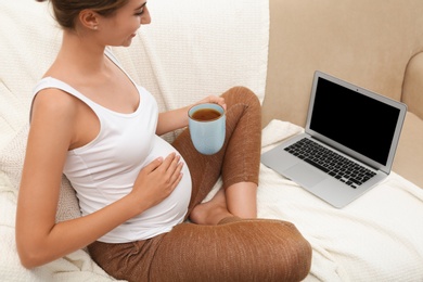 Pregnant woman with laptop drinking tea at home, closeup