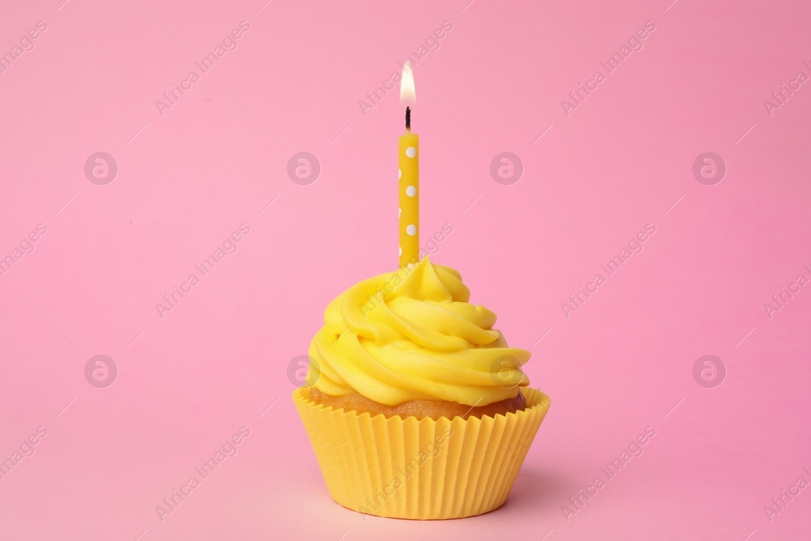 Photo of Delicious birthday cupcake with yellow cream and burning candle on pink background