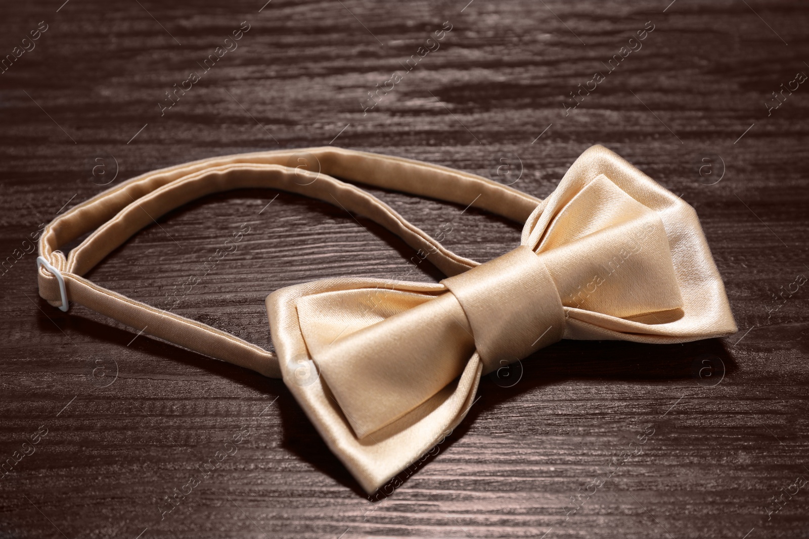 Photo of Stylish beige bow tie on wooden table, closeup