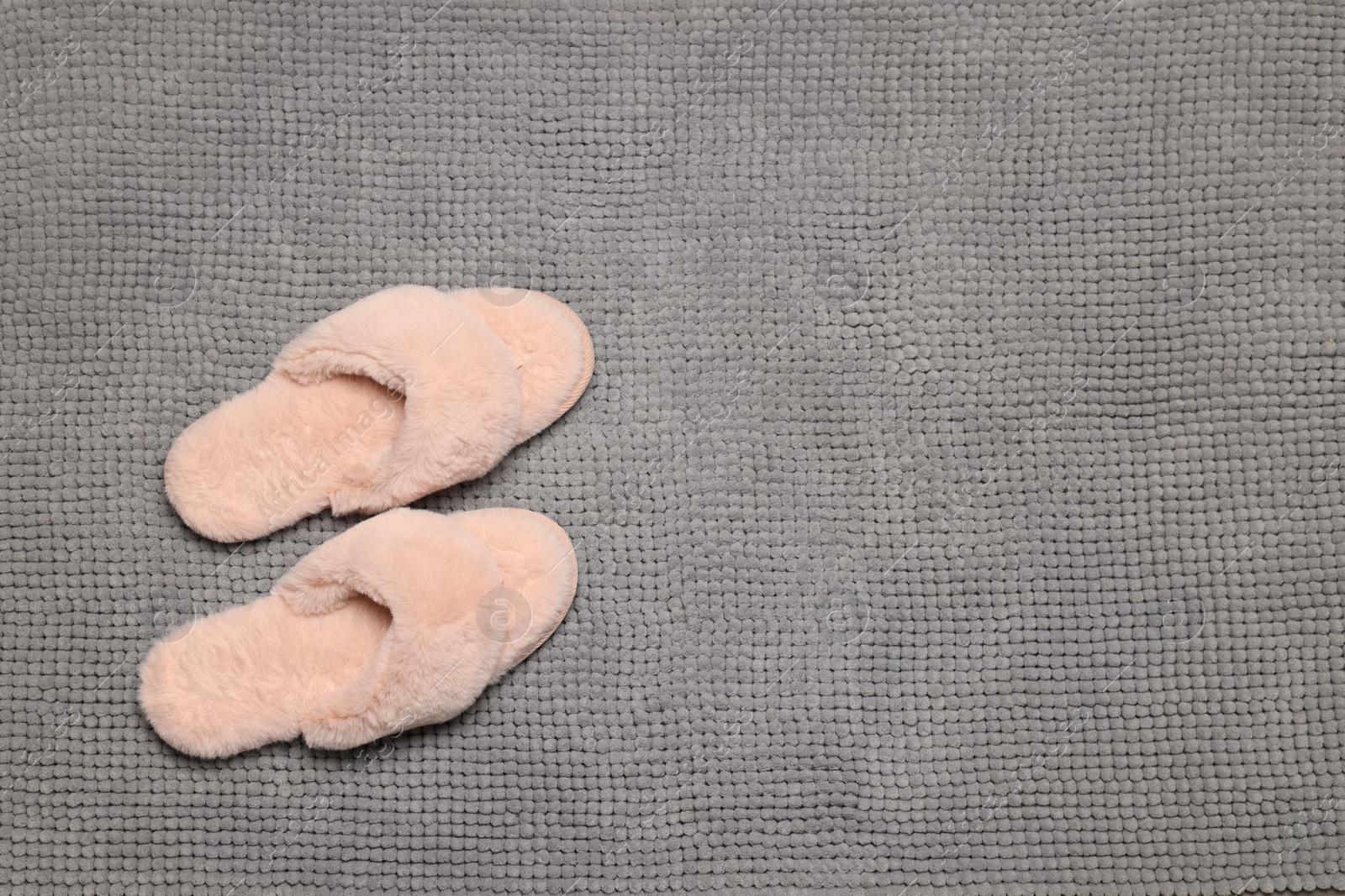 Photo of Slippers on soft grey bath mat, flat lay. Space for text