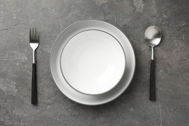 Stylish setting with cutlery and plates on grey textured table, flat lay