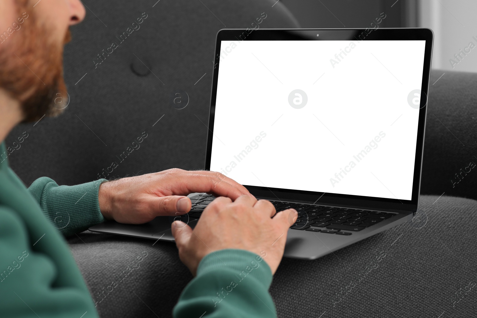 Photo of Man using laptop on grey couch, closeup