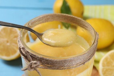 Photo of Taking delicious lemon curd from jar at light blue table, closeup