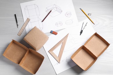 Photo of Creating packaging design. Drawings, boxes and stationery on light wooden table, flat lay