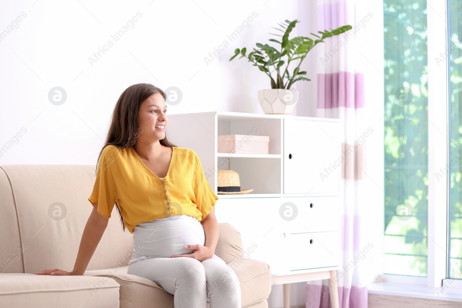 Photo of Pregnant woman sitting on sofa at home