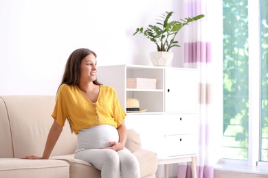 Photo of Pregnant woman sitting on sofa at home