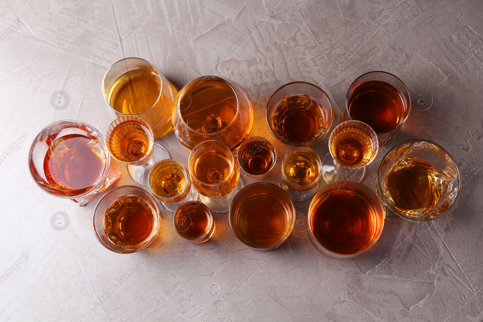 Photo of Many different liqueurs in glasses on grey textured table, flat lay