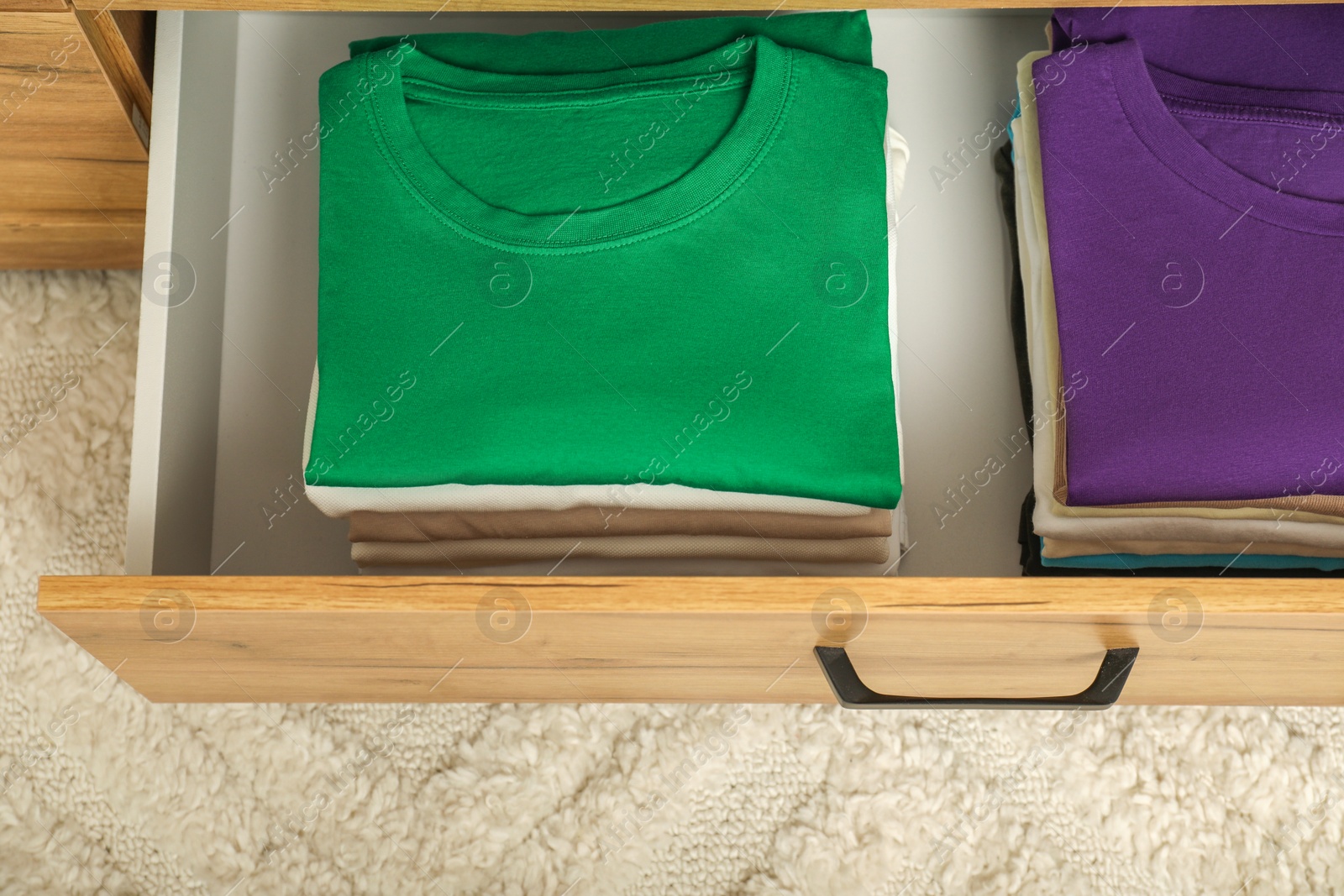Photo of Stacks of different folded shirts in drawer indoors, top view. Organizing clothes