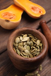 Photo of Mortar with pumpkin seeds on wooden table, closeup