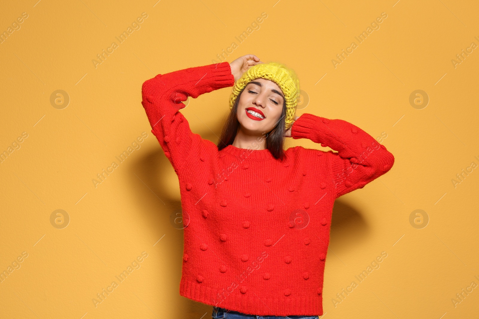 Photo of Young woman in warm sweater and knitted hat on color background. Celebrating Christmas