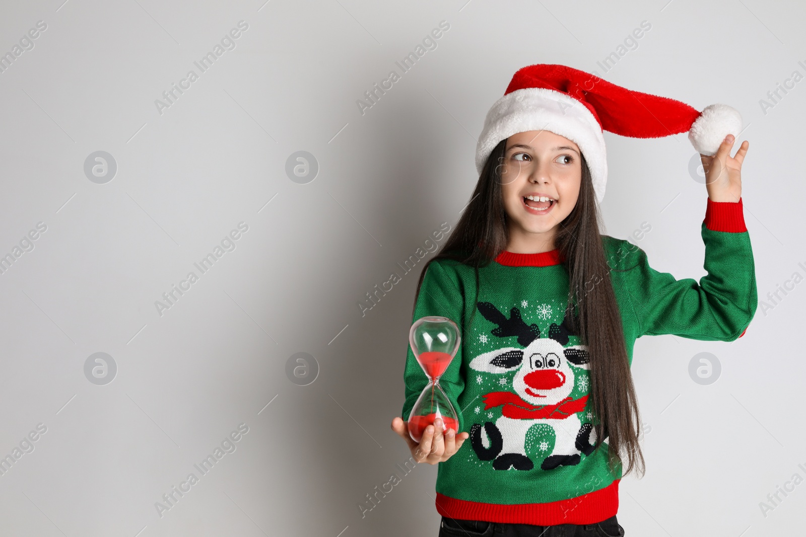Photo of Girl in Santa hat with hourglass on white background, space for text. Christmas countdown
