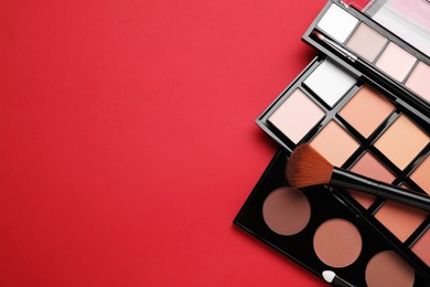 Photo of Colorful contouring palettes and brush on red background, flat lay with space for text. Professional cosmetic product