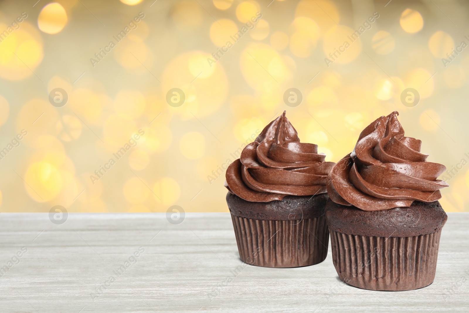 Image of Delicious birthday cupcakes on white wooden table against blurred lights. Space for text