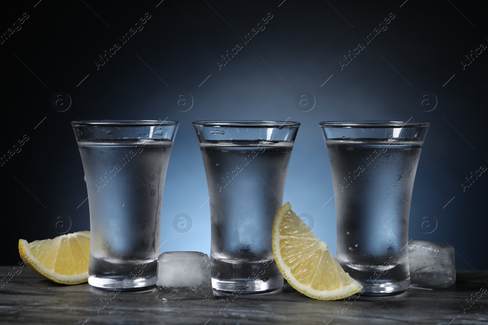 Photo of Shot glasses of vodka with lemon slices and ice on grey table