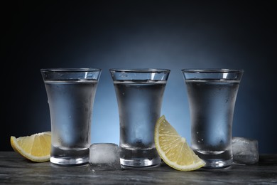 Shot glasses of vodka with lemon slices and ice on grey table