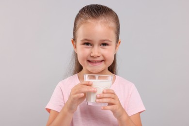 Photo of Cute girl with glass of fresh milk on light grey background