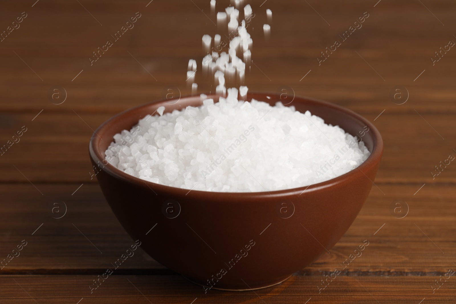 Photo of Natural sea salt falling into bowl on wooden table