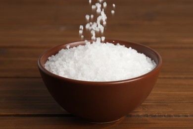 Photo of Natural sea salt falling into bowl on wooden table