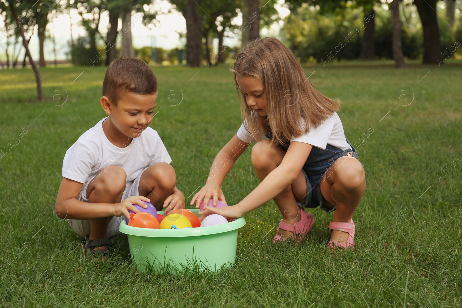 Photo of Little children with basin of water bombs in park