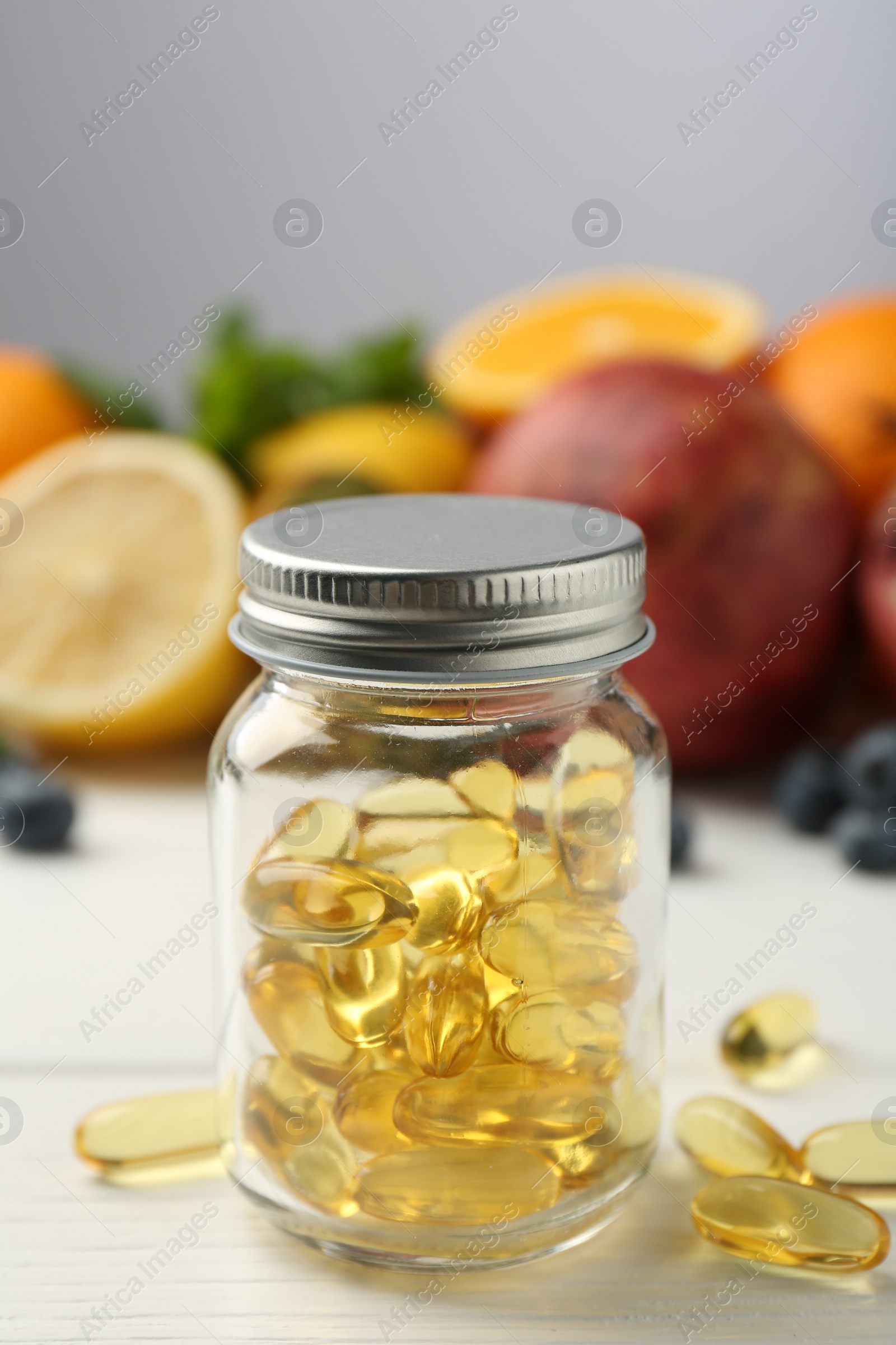 Photo of Vitamin pills in bottle and fresh fruits on white wooden table, closeup